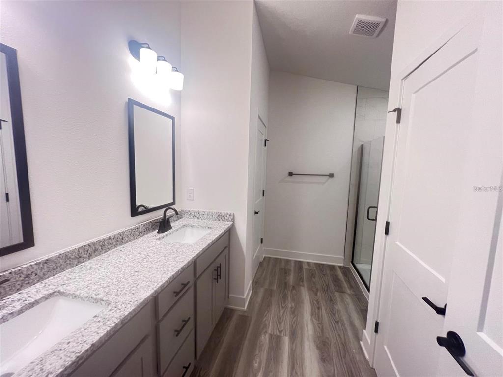 A bathroom features a double vanity with granite countertops, gray cabinets, and a glass shower — 3635 LINDBERGH STREET, LAKELAND, FL