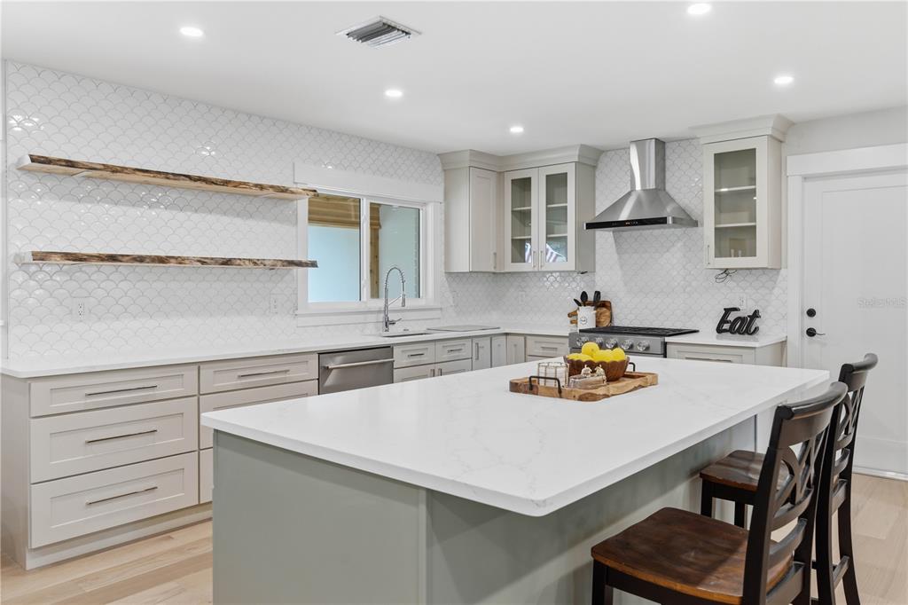 A modern kitchen features a white quartz island, light gray cabinetry, and scalloped tile backsplash — 2218 HENNESEN DRIVE, CLEARWATER, FL