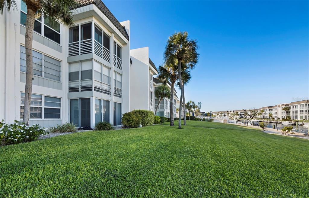 A multi-story apartment building with screened balconies overlooks a grassy lawn and a canal — 4350 CHATHAM DRIVE UNIT 105, LONGBOAT KEY, FL