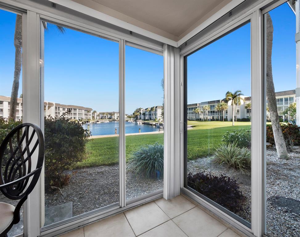 A tiled sunroom features large sliding glass doors overlooking a grassy lawn and a canal — 4350 CHATHAM DRIVE UNIT 105, LONGBOAT KEY, FL