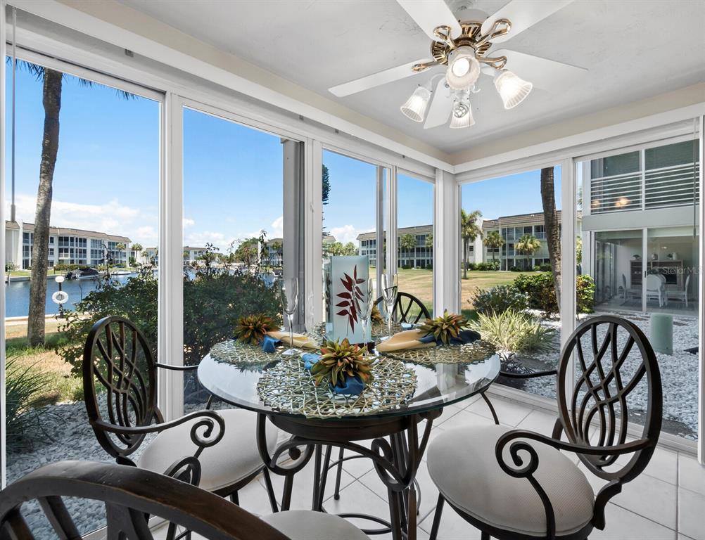 A sunroom with a glass-topped dining table, ceiling fan, and views of a canal — 4350 CHATHAM DRIVE UNIT 105, LONGBOAT KEY, FL