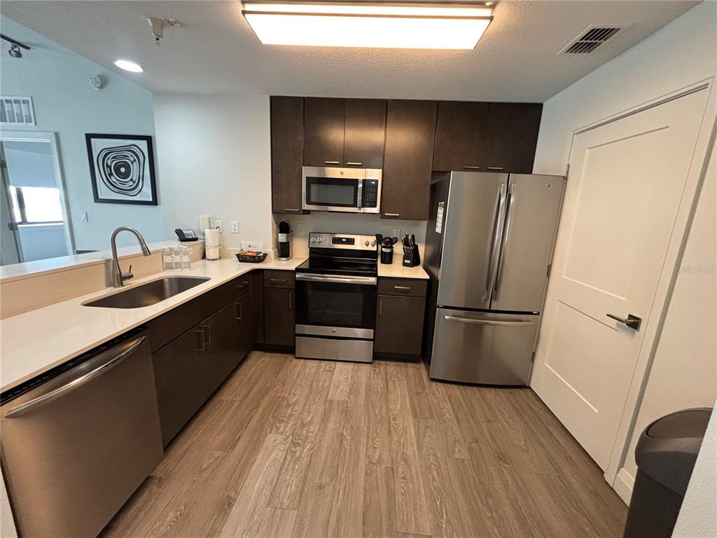 A kitchen features dark cabinetry, stainless steel appliances, white countertops, and light wood-look flooring — 14501 GROVE RESORT AVENUE UNIT 3534, WINTER GARDEN, FL