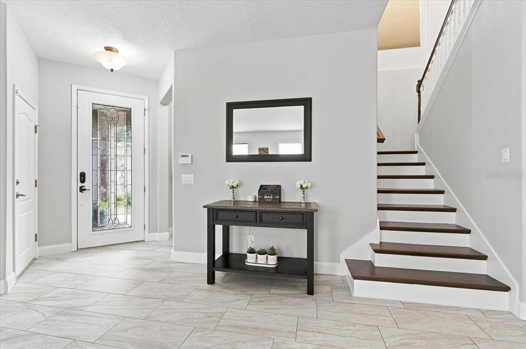 An entryway features light tile flooring, a wooden console table, a mirror, and a staircase — 10908 SUBTLE TRAIL DRIVE, RIVERVIEW, FL