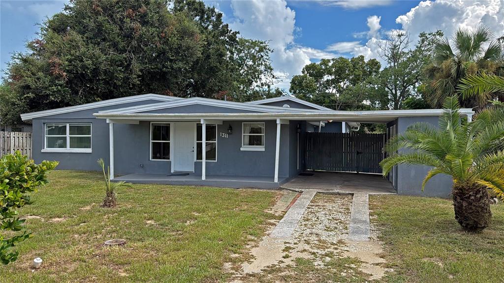 A gray single-story house features a covered front porch, a carport, and a fenced yard — 1311 HILLCREST DRIVE, DAYTONA BEACH, FL