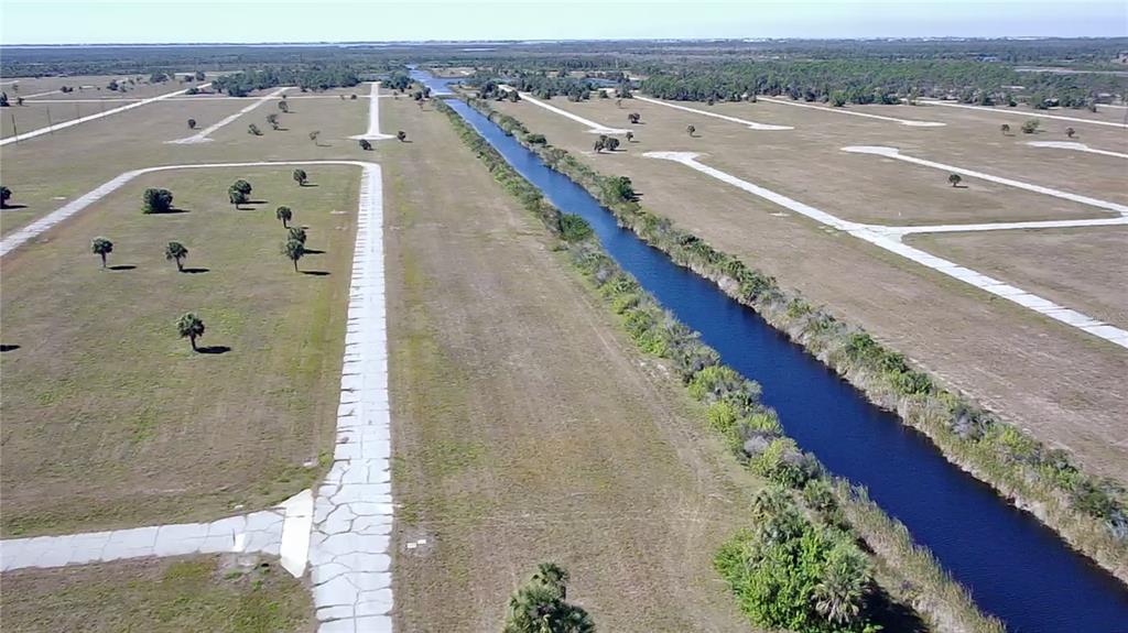 An aerial view shows a canal running through a large, undeveloped residential lot with paved roads — 12295 GREENLING WAY, PLACIDA, FL