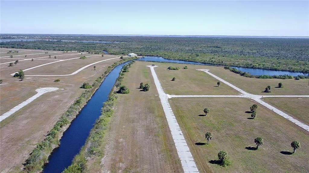 An aerial view shows a canal bordering undeveloped residential lots with paved roads and palm trees — 12295 GREENLING WAY, PLACIDA, FL