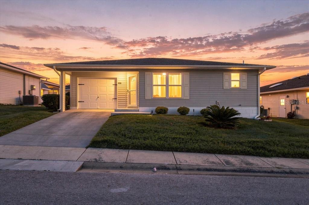 A single-story house with light gray siding, a garage, and a concrete driveway at sunset — 1837 PRAIRIE DUNES CIRCLE S, LAKELAND, FL