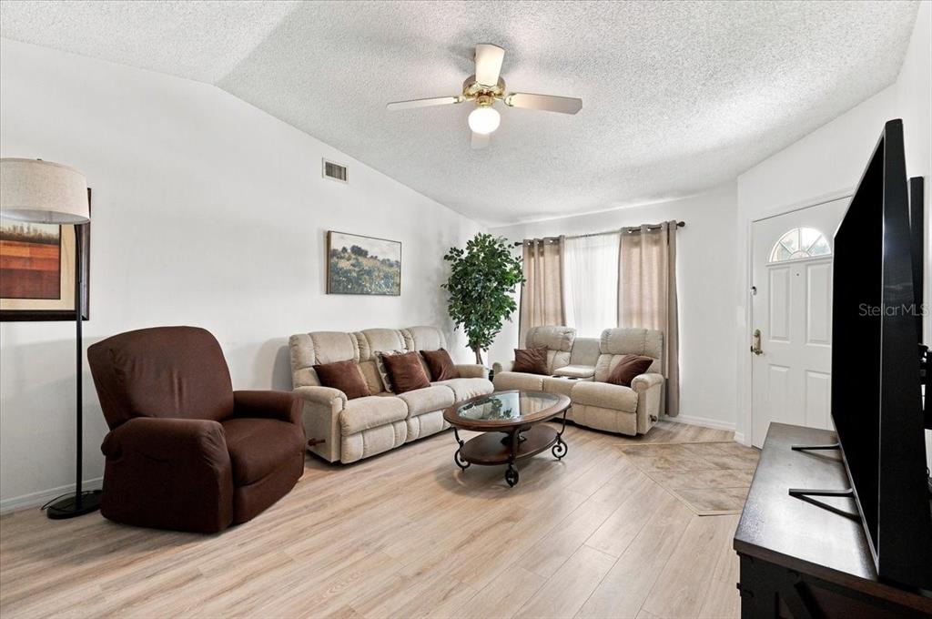 A living room features light wood flooring, a ceiling fan, and neutral-colored furniture — 1837 PRAIRIE DUNES CIRCLE S, LAKELAND, FL