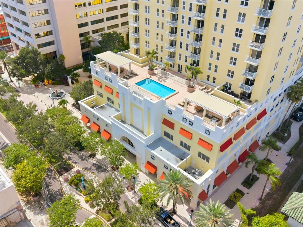 An aerial view shows a yellow multi-story building with a rooftop pool and terrace — 628 CLEVELAND STREET UNIT 1507, CLEARWATER, FL