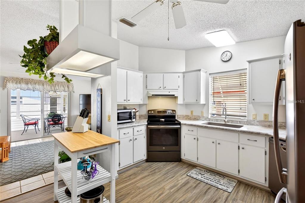 A kitchen features white cabinets, a wood-topped island, and stainless steel appliances on wood flooring — 932 CHULA CT, LADY LAKE, FL