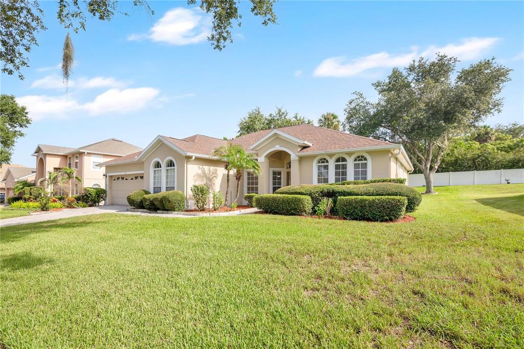 A single-story suburban house with a tan stucco exterior, arched windows, and a manicured lawn — 253 BEACON POINTE DRIVE, OCOEE, FL