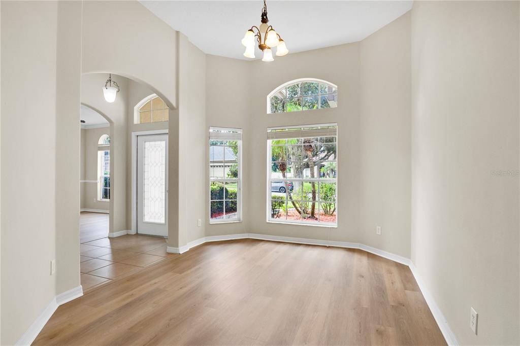 An empty room with light wood-look flooring, high ceilings, large windows, and a chandelier — 253 BEACON POINTE DRIVE, OCOEE, FL