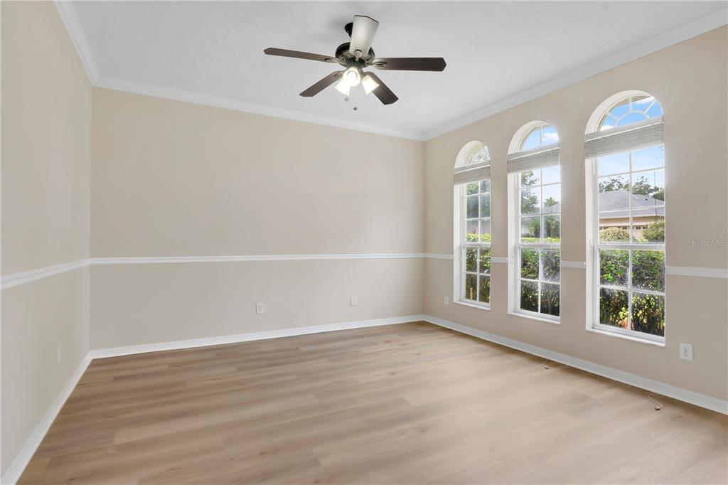 An empty room with light wood-look flooring, beige walls, chair rail molding, and three arched windows — 253 BEACON POINTE DRIVE, OCOEE, FL