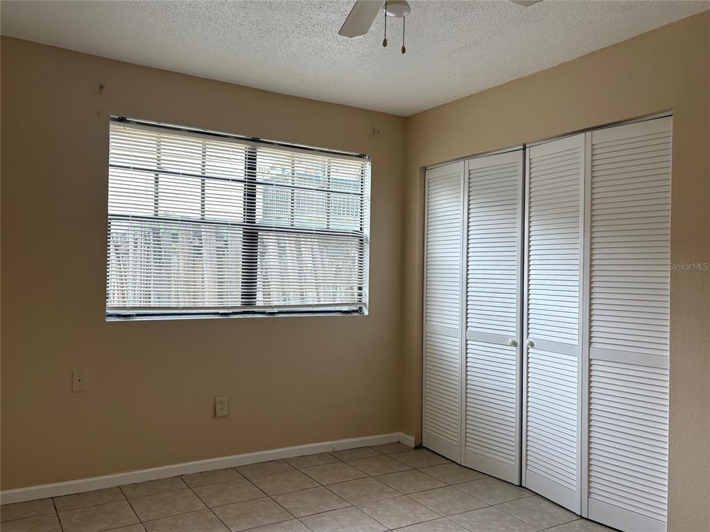 A bedroom features beige walls, tile flooring, a window with blinds, and white louvered closet doors — 203 POINSETTIA PINE COURT UNIT 102, TAMPA, FL