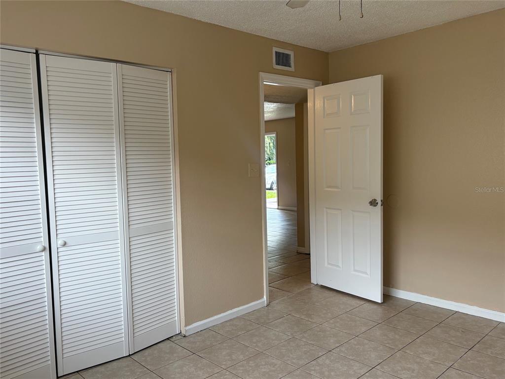A room with beige walls, tiled flooring, white louvered closet doors, and an open doorway — 203 POINSETTIA PINE COURT UNIT 102, TAMPA, FL