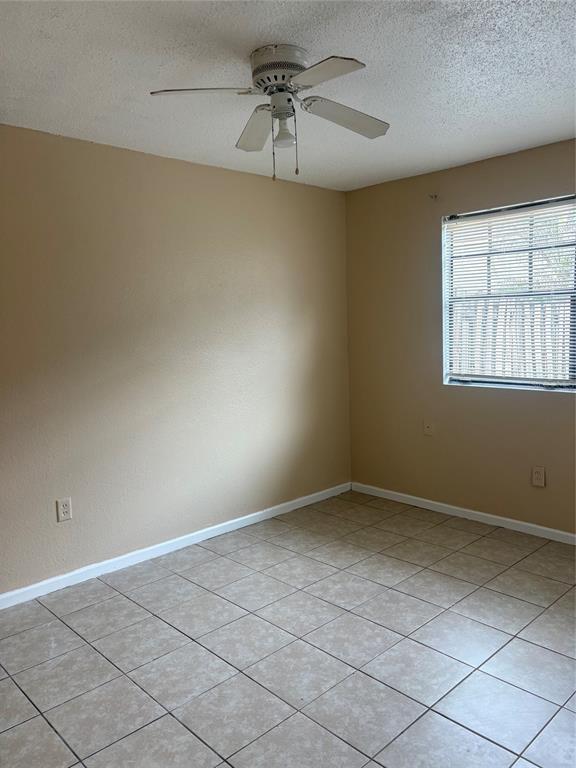 An empty room features tan walls, a white ceiling fan, and light-colored tile flooring — 203 POINSETTIA PINE COURT UNIT 102, TAMPA, FL