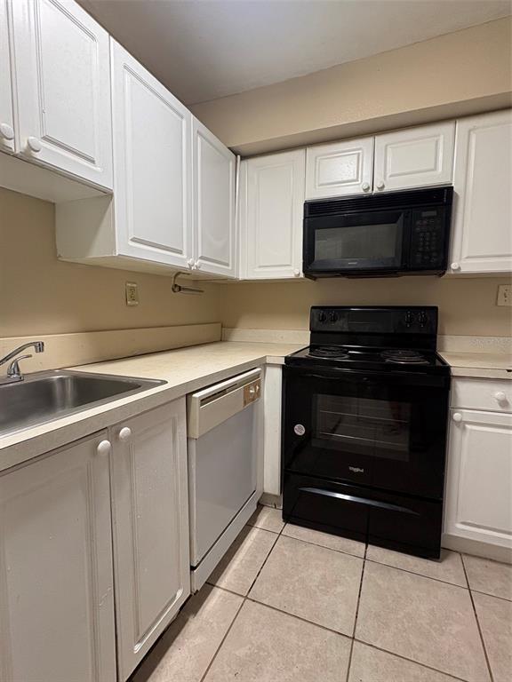 A kitchen features white cabinets, a black stove and microwave, a dishwasher, and tile flooring — 203 POINSETTIA PINE COURT UNIT 102, TAMPA, FL