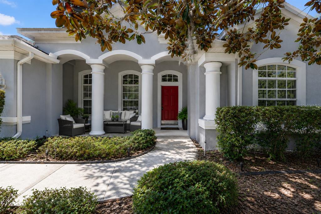 A gray house exterior features a red front door, white columns, and a covered porch — 1603 GRAND HERITAGE BOULEVARD, VALRICO, FL