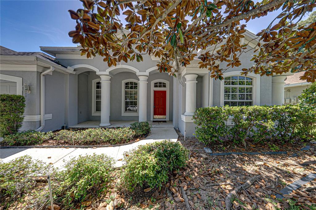 A gray house exterior features a red front door, arched columns, and a landscaped yard — 1603 GRAND HERITAGE BOULEVARD, VALRICO, FL