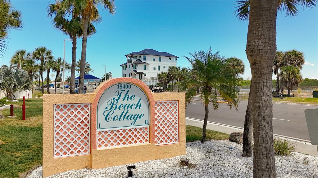 A sign for The Beach Cottage stands in a landscaped area with palm trees nearby — 18400 GULF BOULEVARD UNIT 1108, INDIAN SHORES, FL