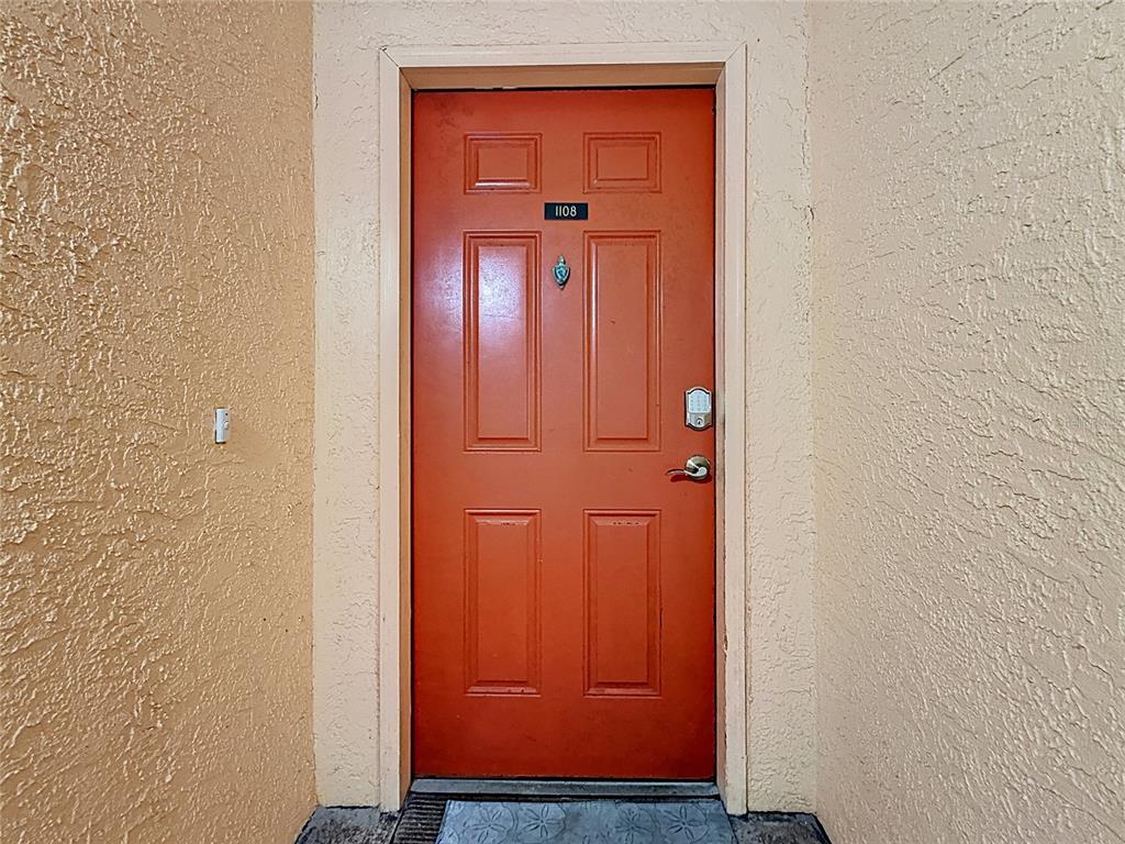 An orange front door with the number 1108 is set into a textured beige wall — 18400 GULF BOULEVARD UNIT 1108, INDIAN SHORES, FL