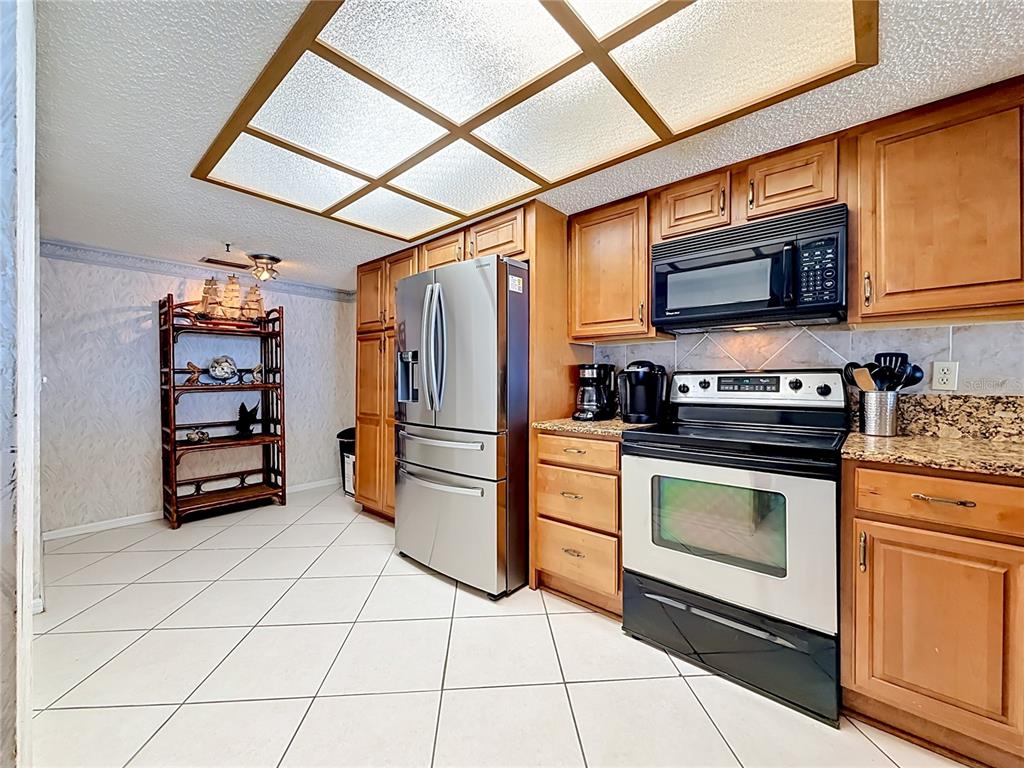 A kitchen with wood cabinets, stainless steel appliances, granite countertops, and a grid ceiling light — 18400 GULF BOULEVARD UNIT 1108, INDIAN SHORES, FL