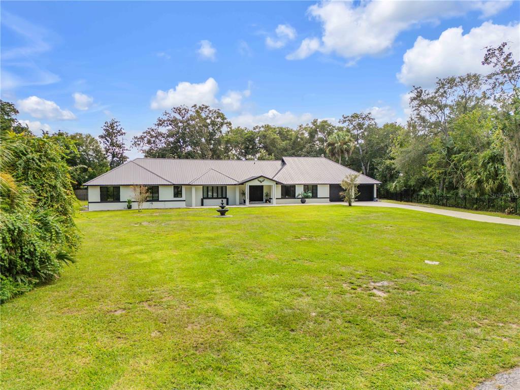 A single-story house with a metal roof and a long concrete driveway sits on grass — 6223 DONNA CIRCLE, PORT ORANGE, FL