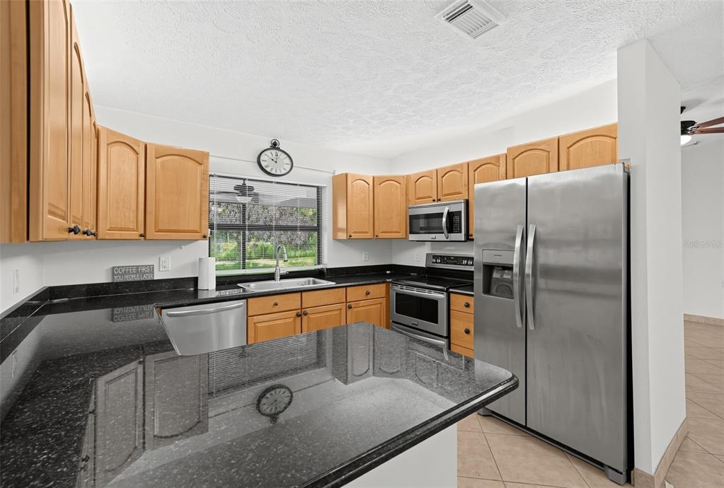 A kitchen features light wood cabinets, black granite countertops, and stainless steel appliances — 3951 SW CHERIBON STREET, PORT ST LUCIE, FL