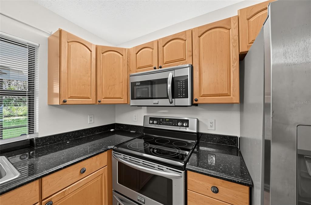 A kitchen features light wood cabinets, black granite countertops, and stainless steel appliances — 3951 SW CHERIBON STREET, PORT ST LUCIE, FL