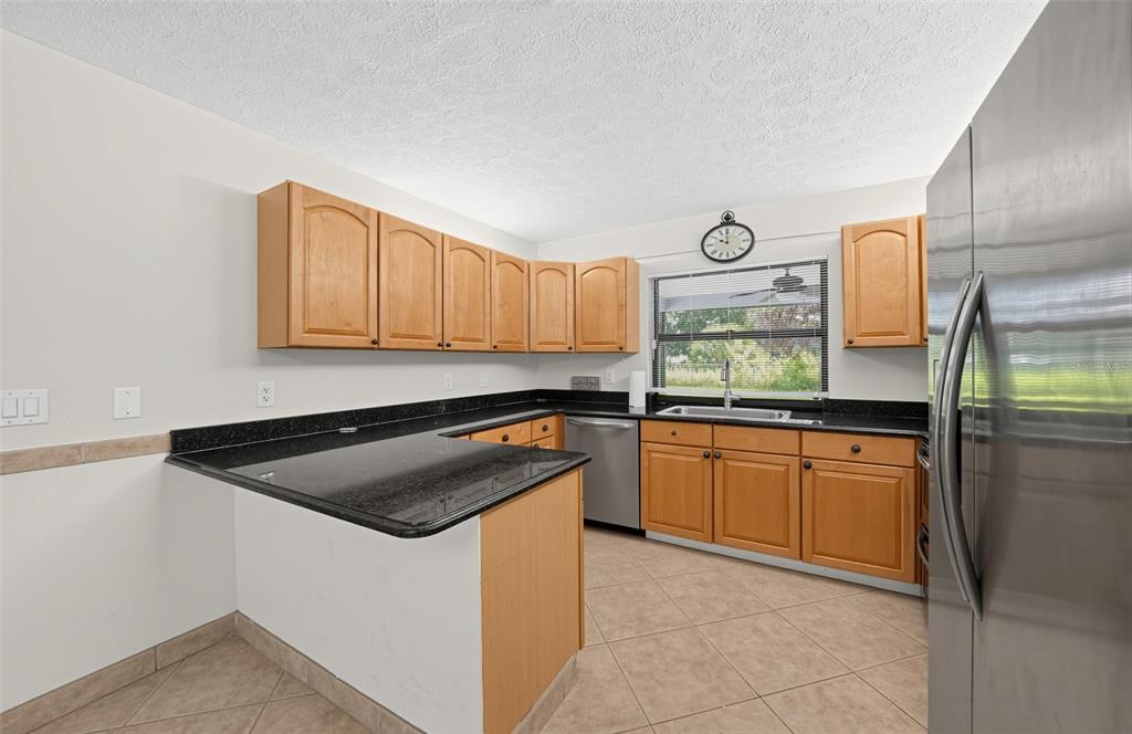 A kitchen features light wood cabinets, black countertops, stainless steel appliances, and beige tile flooring — 3951 SW CHERIBON STREET, PORT ST LUCIE, FL
