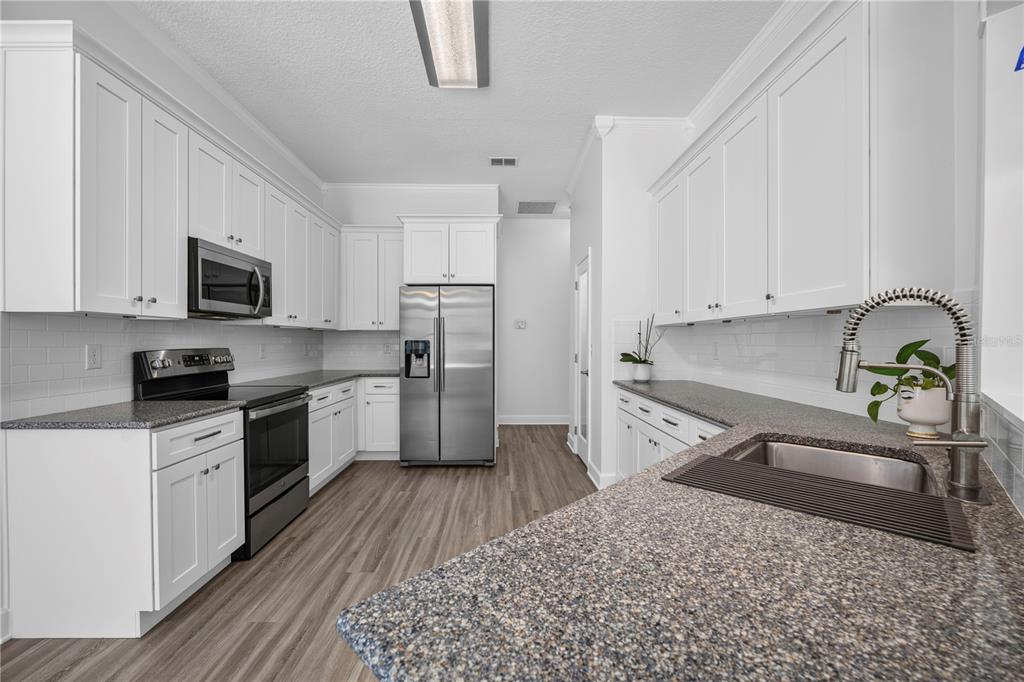 A kitchen with white cabinets, stainless steel appliances, granite countertops, and wood-look flooring — 656 WYNDHAM COURT, ORANGE PARK, FL