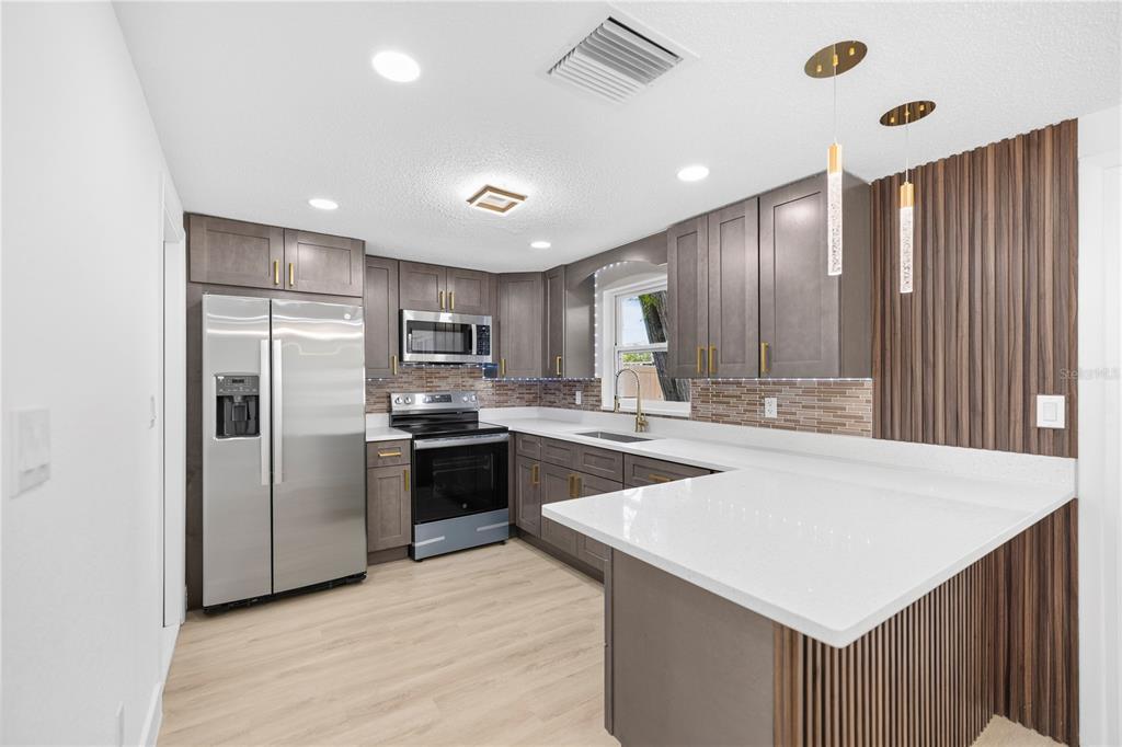 A modern kitchen features gray cabinets, stainless steel appliances, white countertops, and wood-slat accent walls — 6444 JUNIPER ROAD, PORT RICHEY, FL
