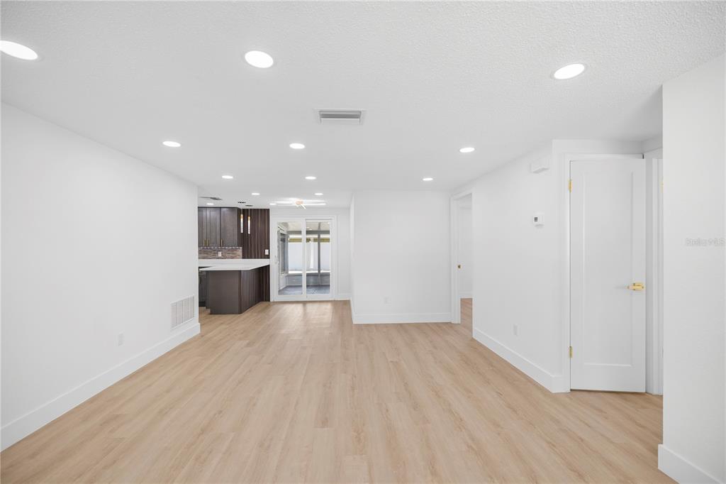 A bright, open-concept living area features light wood-look flooring, recessed lighting, and a modern kitchen — 6444 JUNIPER ROAD, PORT RICHEY, FL