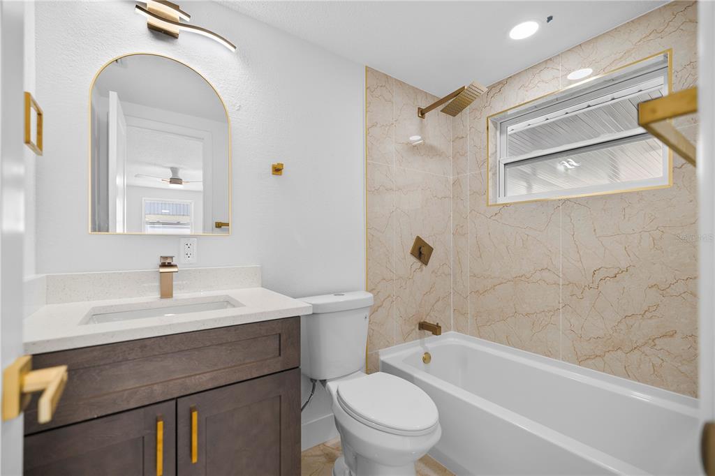 A bathroom features a dark wood vanity, arched mirror, and a tub with marble-look tile — 6444 JUNIPER ROAD, PORT RICHEY, FL