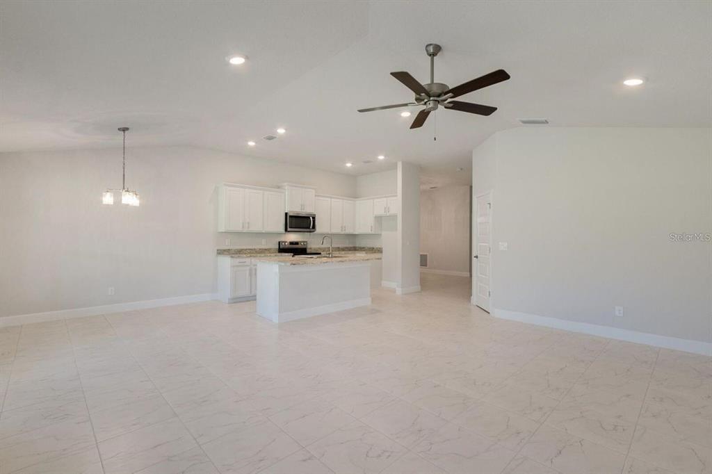 An open-concept kitchen with white cabinets and a granite island overlooks a large tiled room — 4404 SW 92ND PLACE ROAD, OCALA, FL