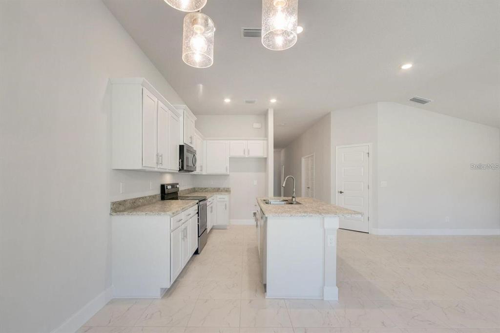 A modern kitchen features white cabinetry, granite countertops, a center island, and tile flooring — 4404 SW 92ND PLACE ROAD, OCALA, FL