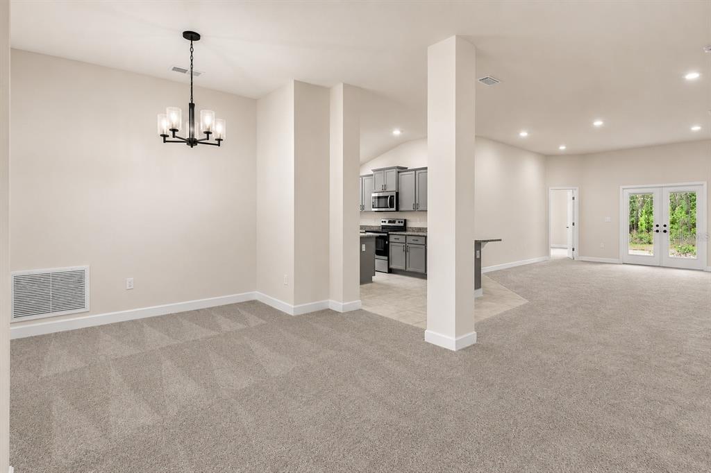 A dining area with a chandelier leads to a kitchen with gray cabinets and carpeted floors — 1667 ANN ROSE WAY, LEESBURG, FL