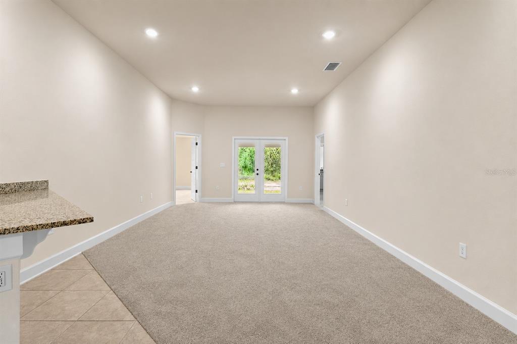 A carpeted living room features recessed lighting, beige walls, and double glass doors leading outside — 1667 ANN ROSE WAY, LEESBURG, FL