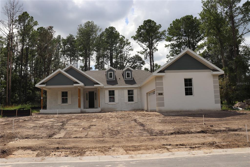 A newly constructed single-story house with a white brick facade, gray siding, and a garage — 5063 ELM LEAF DRIVE, BROOKSVILLE, FL