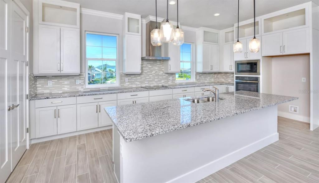 A modern kitchen features white cabinetry, granite countertops, a central island, and light wood-look flooring — 23 MARDEN DRIVE UNIT 51, ORMOND BEACH, FL