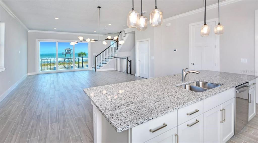 A kitchen island with granite countertops overlooks a living area with a staircase and ocean view — 23 MARDEN DRIVE UNIT 51, ORMOND BEACH, FL