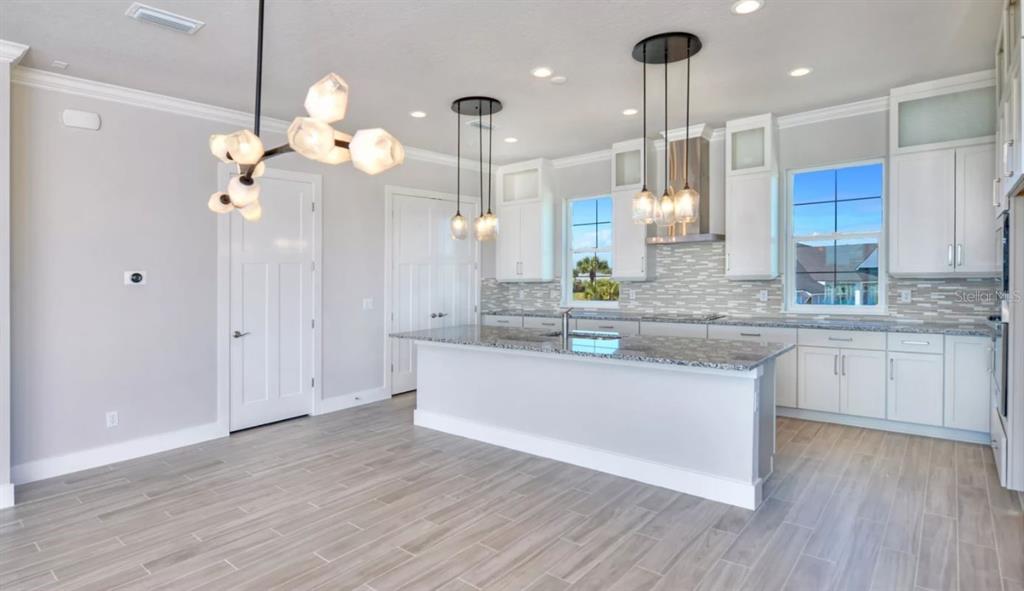 A modern kitchen features white cabinetry, granite countertops, a central island, and wood-look tile flooring — 23 MARDEN DRIVE UNIT 51, ORMOND BEACH, FL