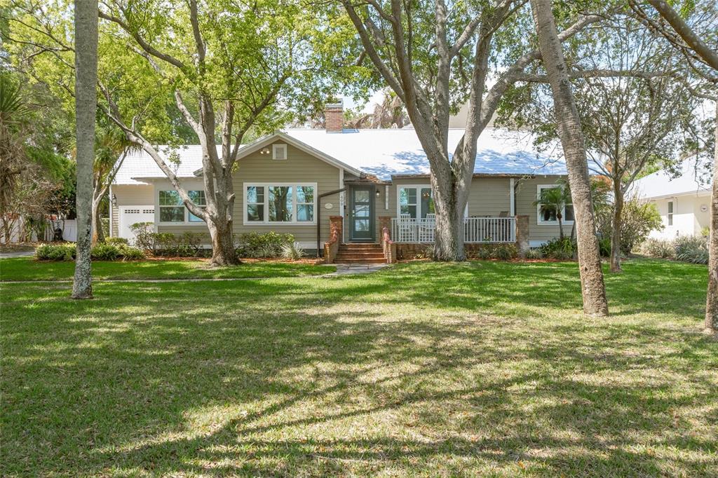 A single-story house with tan siding, a white roof, and a front porch among trees — 409 ROCKLEDGE DRIVE, ROCKLEDGE, FL