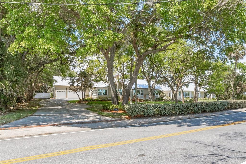 A single-story house with a white garage and a large driveway sits behind mature trees — 409 ROCKLEDGE DRIVE, ROCKLEDGE, FL