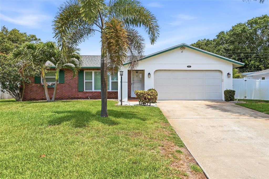A single-story house with a brick and white exterior, a two-car garage, and a palm tree — 14161 HETRICK CIRCLE N, LARGO, FL