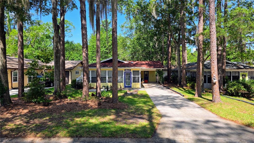 A yellow house with a screened-in front porch and a concrete driveway sits among trees — 8496 NW 38TH TERRACE, GAINESVILLE, FL