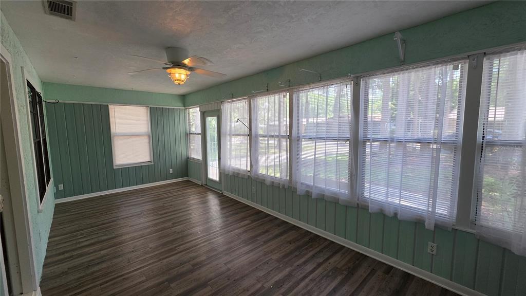 A sunroom features light green paneled walls, a ceiling fan, and virtual staging furniture — 8496 NW 38TH TERRACE, GAINESVILLE, FL