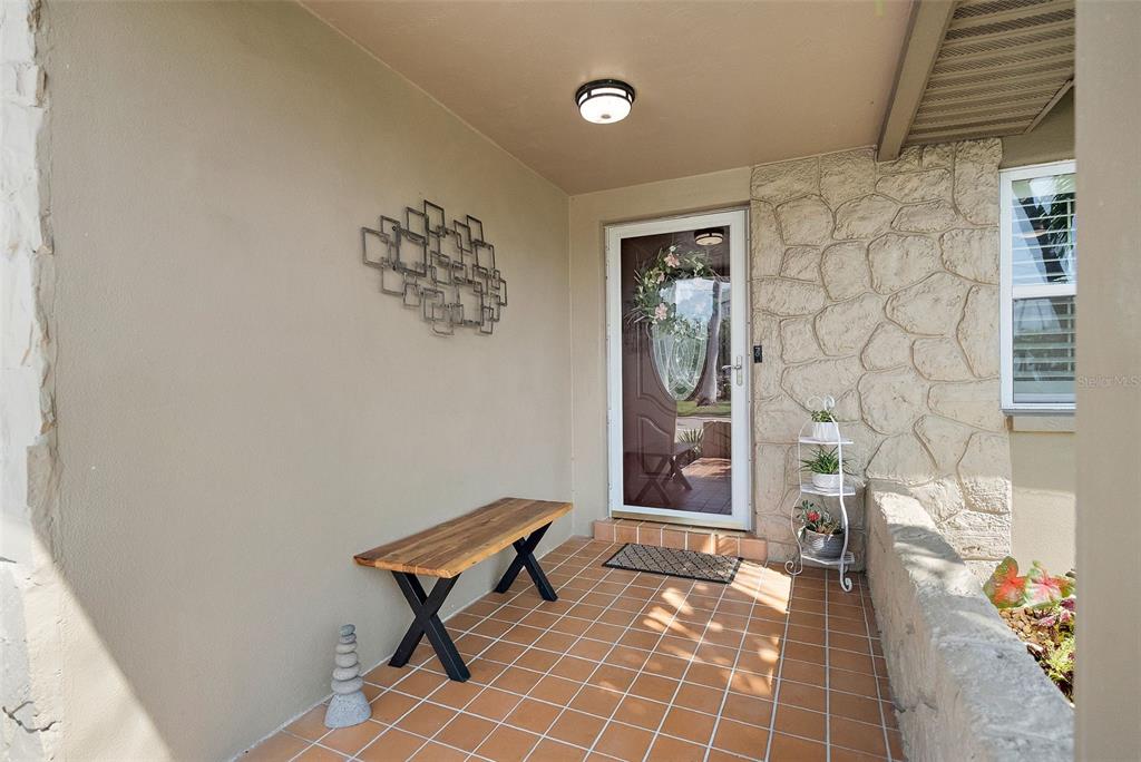 A covered front porch features a wooden bench, tiled floor, and stone wall accents — 101 MADONNA BOULEVARD, TIERRA VERDE, FL
