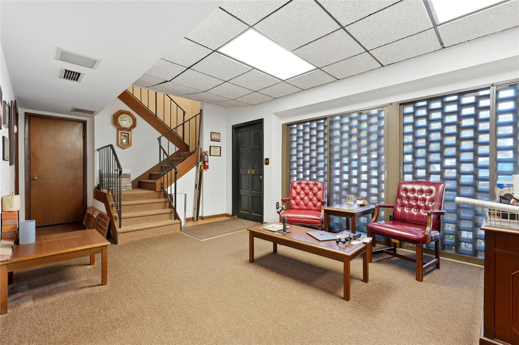 A carpeted room features a staircase, a drop ceiling, and two red leather armchairs — 711 NW 23RD AVENUE UNIT 3, GAINESVILLE, FL