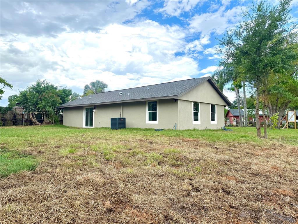The rear exterior of a single-story house with a yard and an air conditioning unit — 1427 MURILLO LOOP, RUSKIN, FL